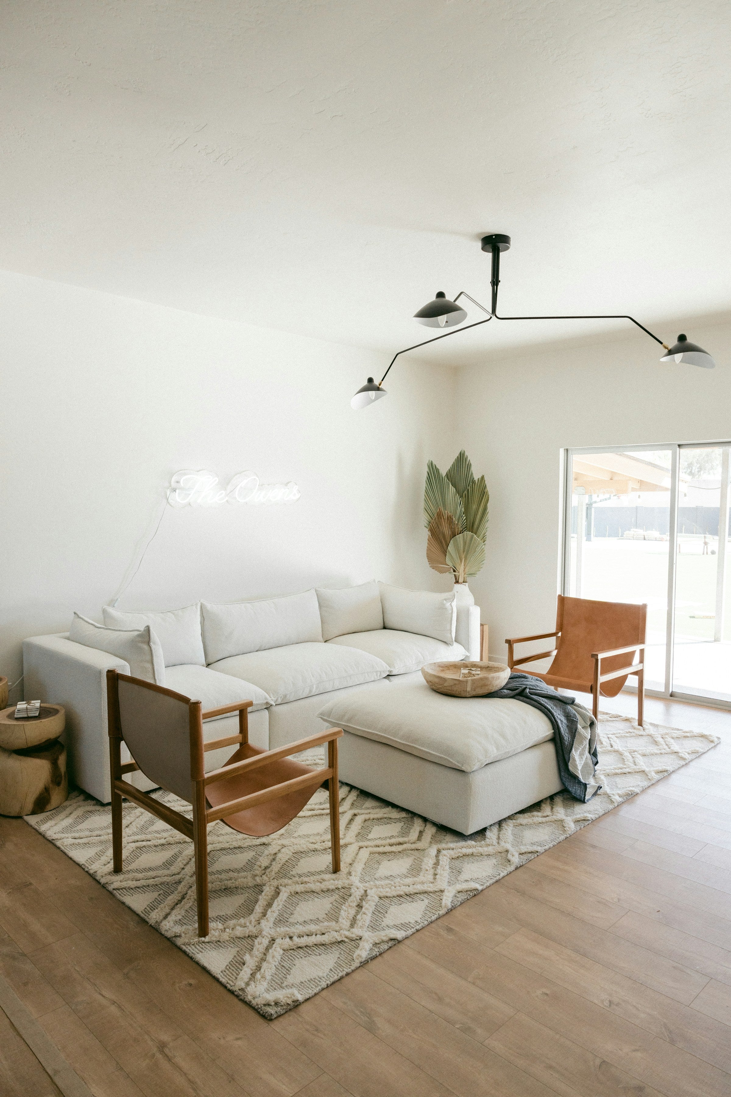 Well-lit living room featuring a central sofa and table, with a mattress and a vase of flowers nearby.